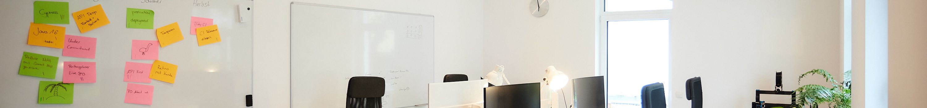 Ein Büroraum mit zwei Whiteboards an der Wand. An einem Whiteboard hängen bunte Post its, die gruppiert und sortiert sind.