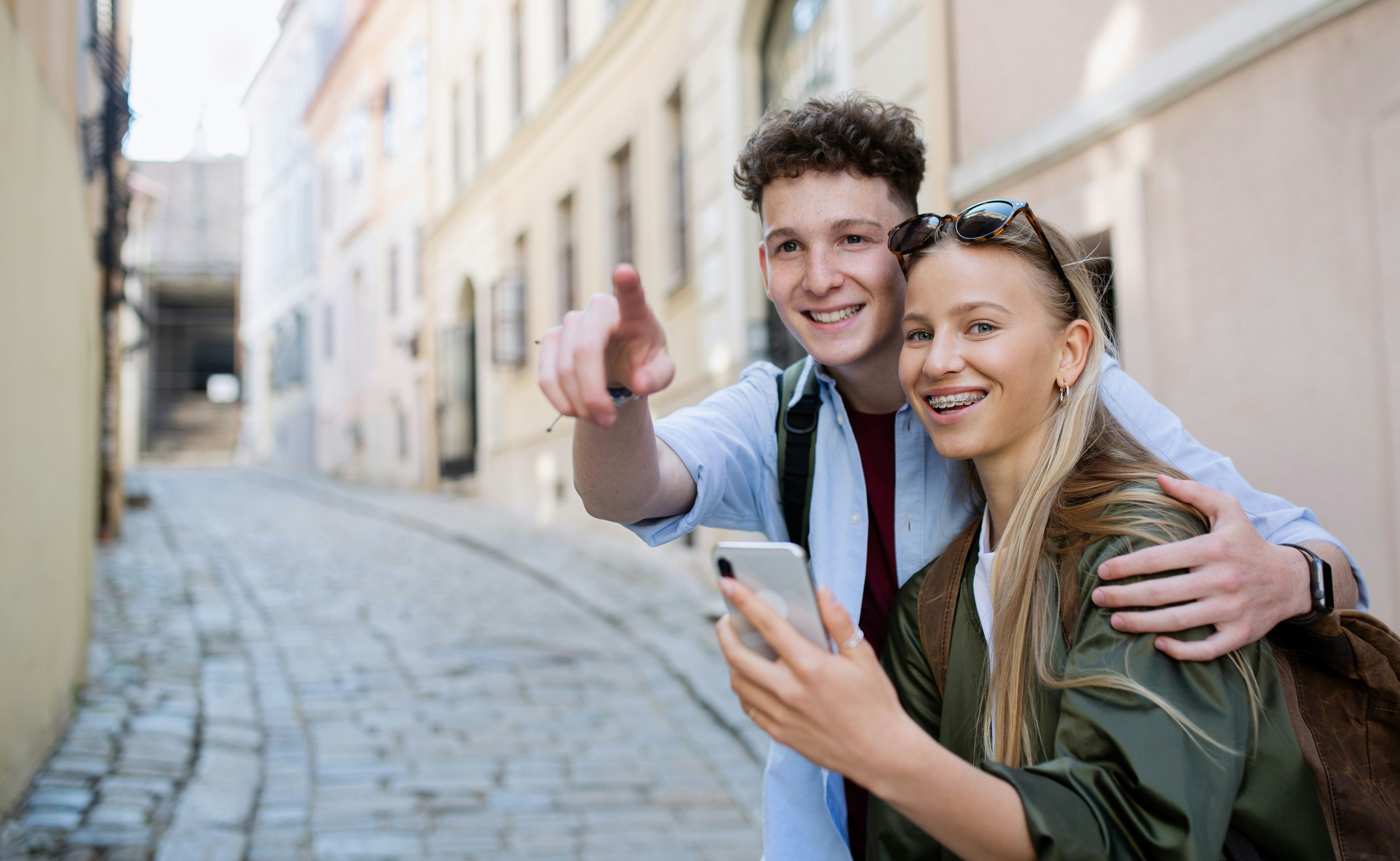 Junges Paar zusammen in einer Stadt. Die Frau hat ein Handy in der Hand und der Mann zeigt nach vorne.